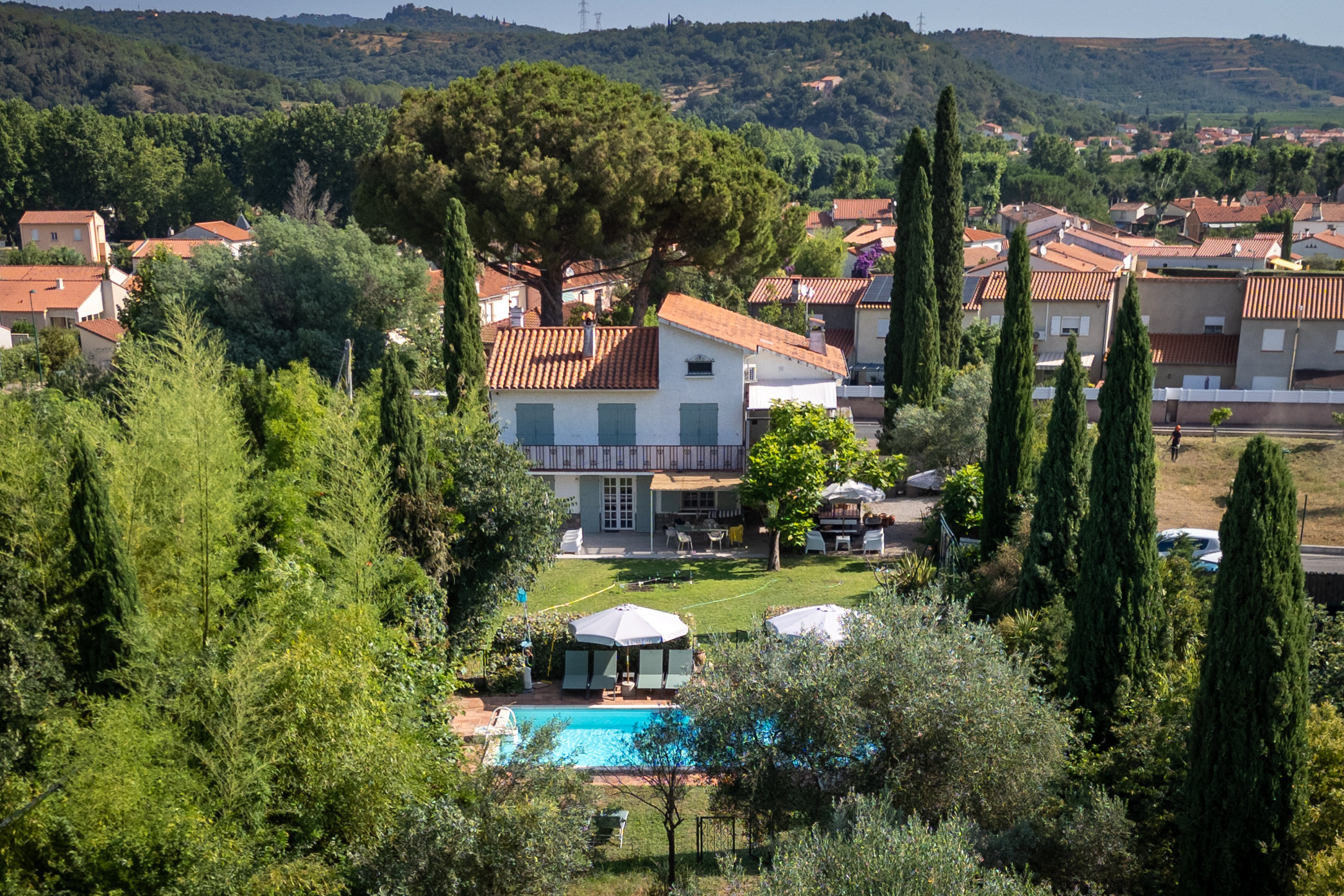 Luftaufnahme der Villa Alosa mit Pool und Garten, dahinter Céret und die bewaldeten Hügel
